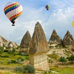 Colorful hot air balloons flying over volcanic cliffs at Cappadocia, Anatolia, Turkey.