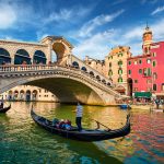 Colorful morning view of Rialto Bridge. Amazing cityscape of  Venice with tourists on gondolas, Italy, Europe. Romantic summer scene of famous Canal Grande. Traveling concept background.